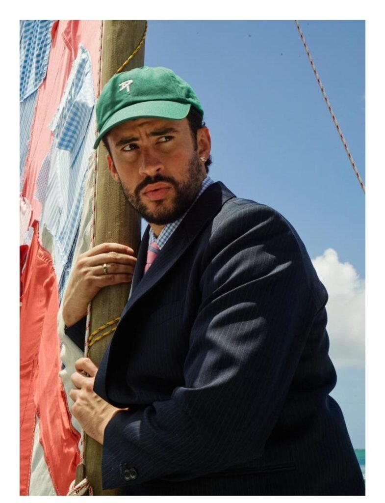 Bad Bunny con traje oscuro y gorra verde en una campaña editorial de moda inspirada en Zara junto al mar