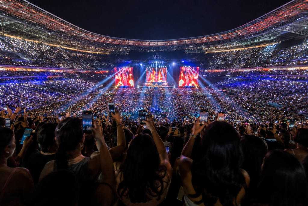 Vista panorámica de un estadio repleto de asistentes durante un gran concierto de Bad Bunny en Madrid, con miles de luces iluminando la noche y un ambiente festivo internacional.