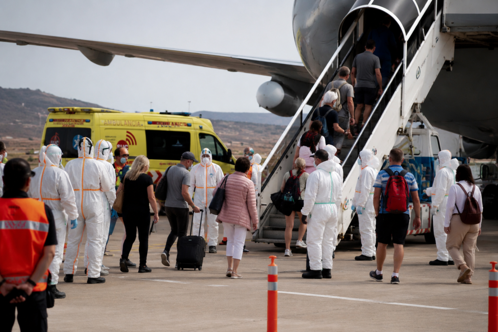 Pasajeros del crucero MV Hondius siendo repatriados en un aeropuerto mientras sanitarios con EPIs supervisan el embarque tras el brote de hantavirus.